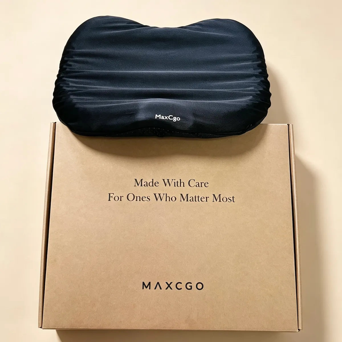 A dark navy blue contoured pillow resting on top of its kraft paper packaging box. The box features the brand name 'MAXCGO' and the text 'Made With Care For Ones Who Matter Most'.