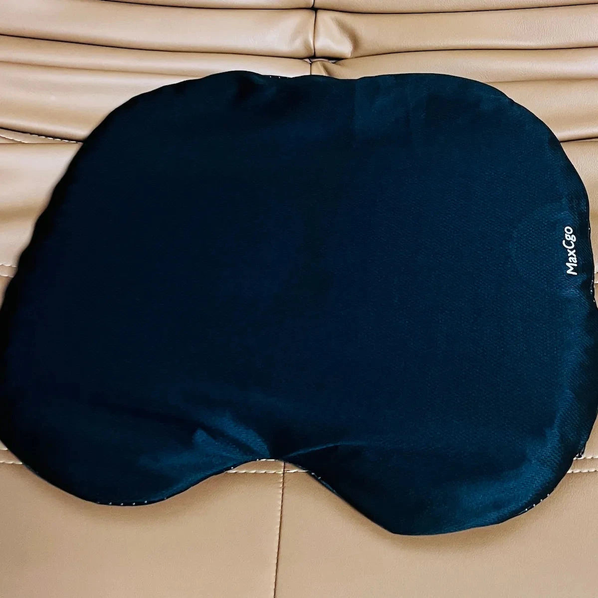 A dark navy blue fabric seat cushion or lumbar support pad with a small white 'MaxCep' logo on the right side, laid flat on a beige leather surface.