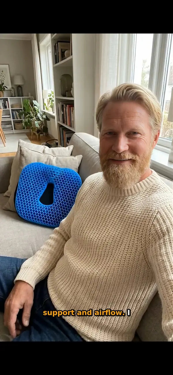 A man with blond hair and a beard sits on a beige sofa in a bright living room, wearing a cream knit sweater. A bright blue contoured pillow is visible behind him.